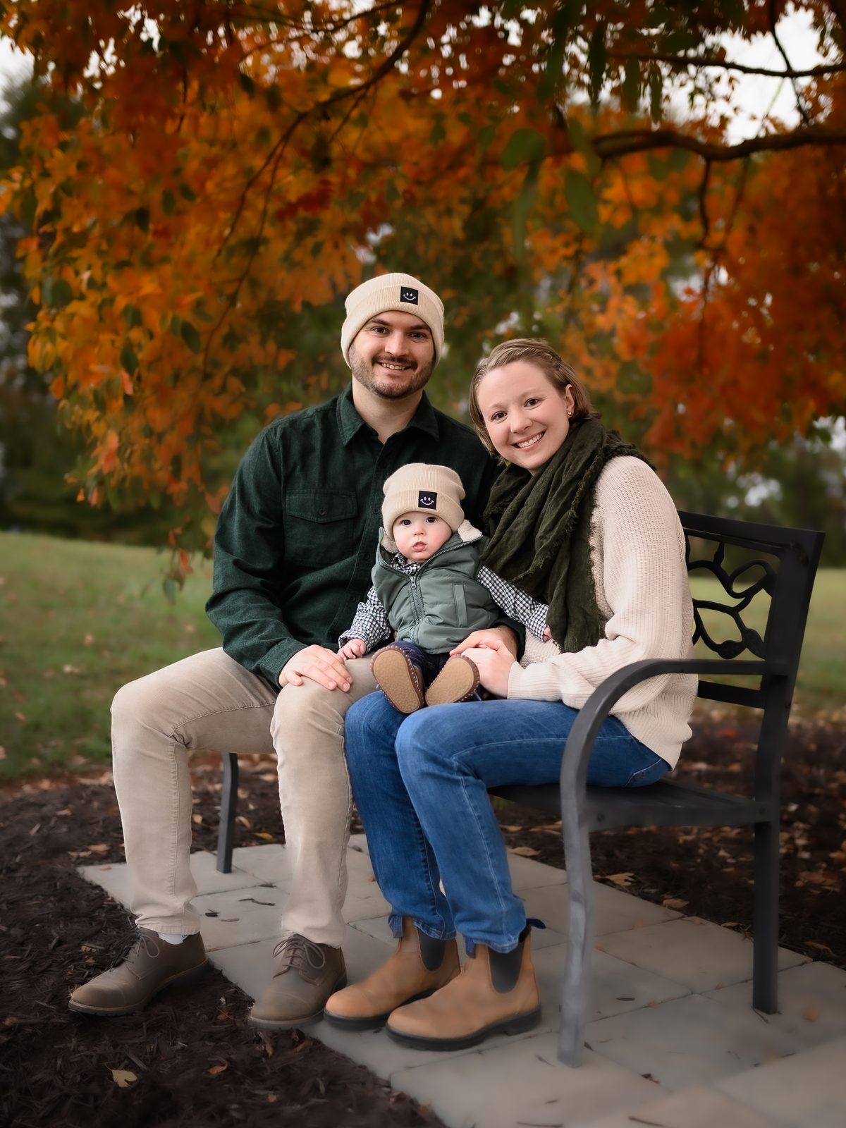 Jacob and Lily Rigmaiden with their child, on a bench under fall foliage